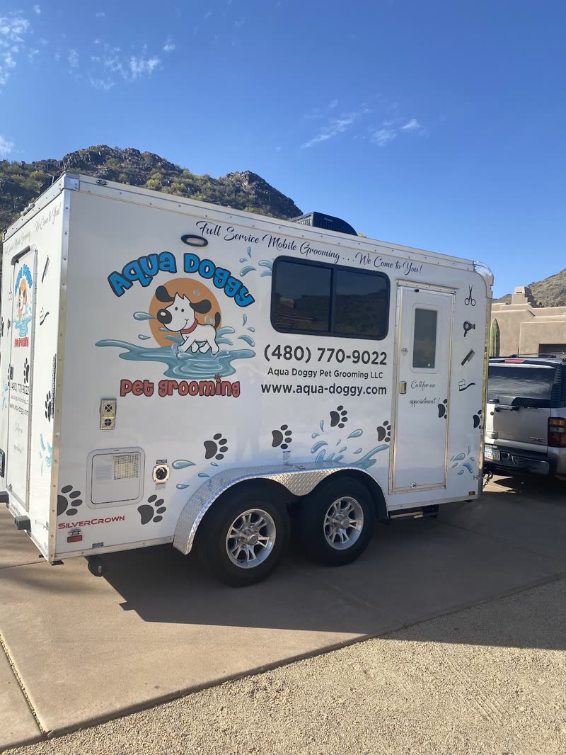 The white Aqua Doggy grooming trailer parked on a driveway with mountains behind it